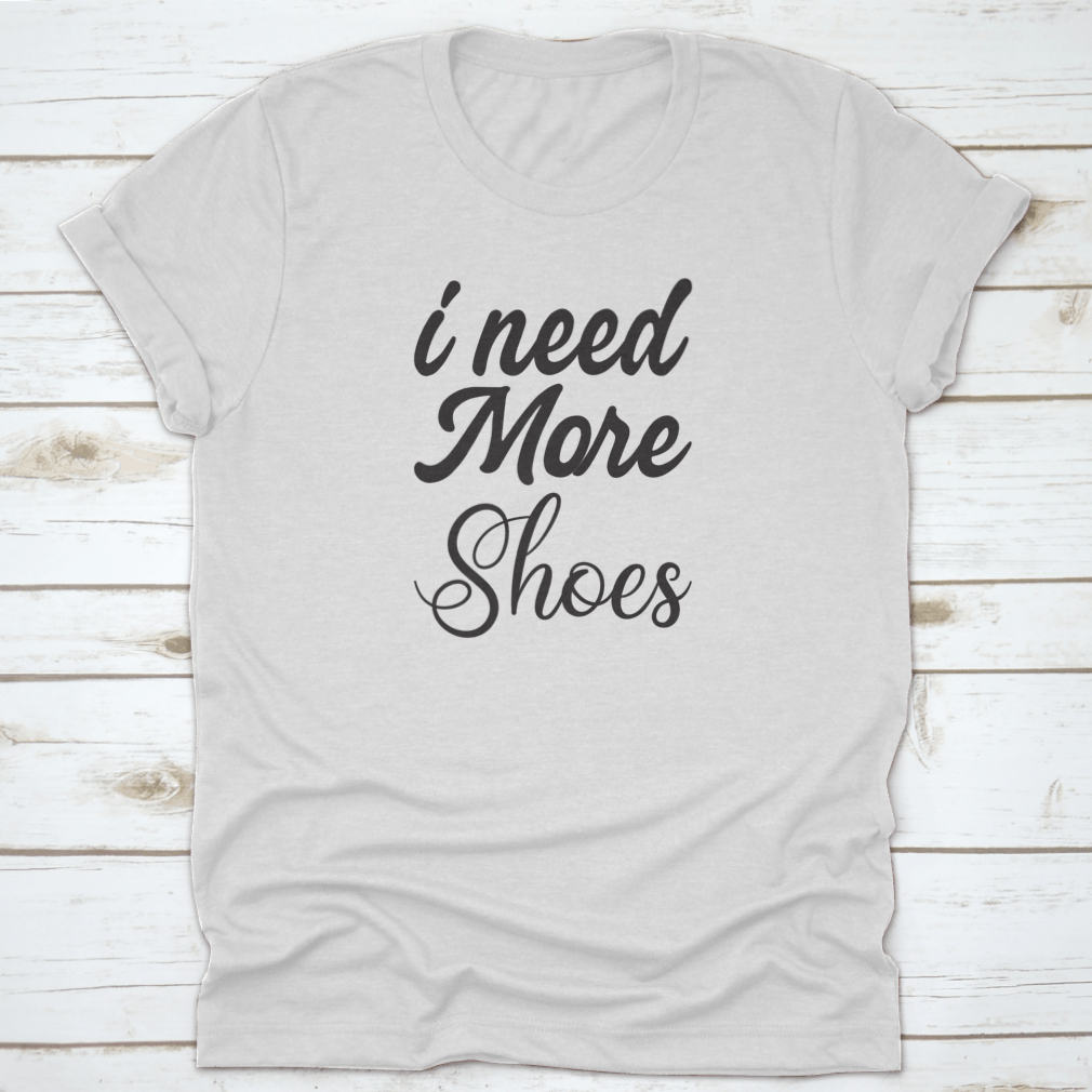 A stylish grey T-shirt featuring the quote 'I Need More Shoes' in bold letters, made from soft cotton fabric.