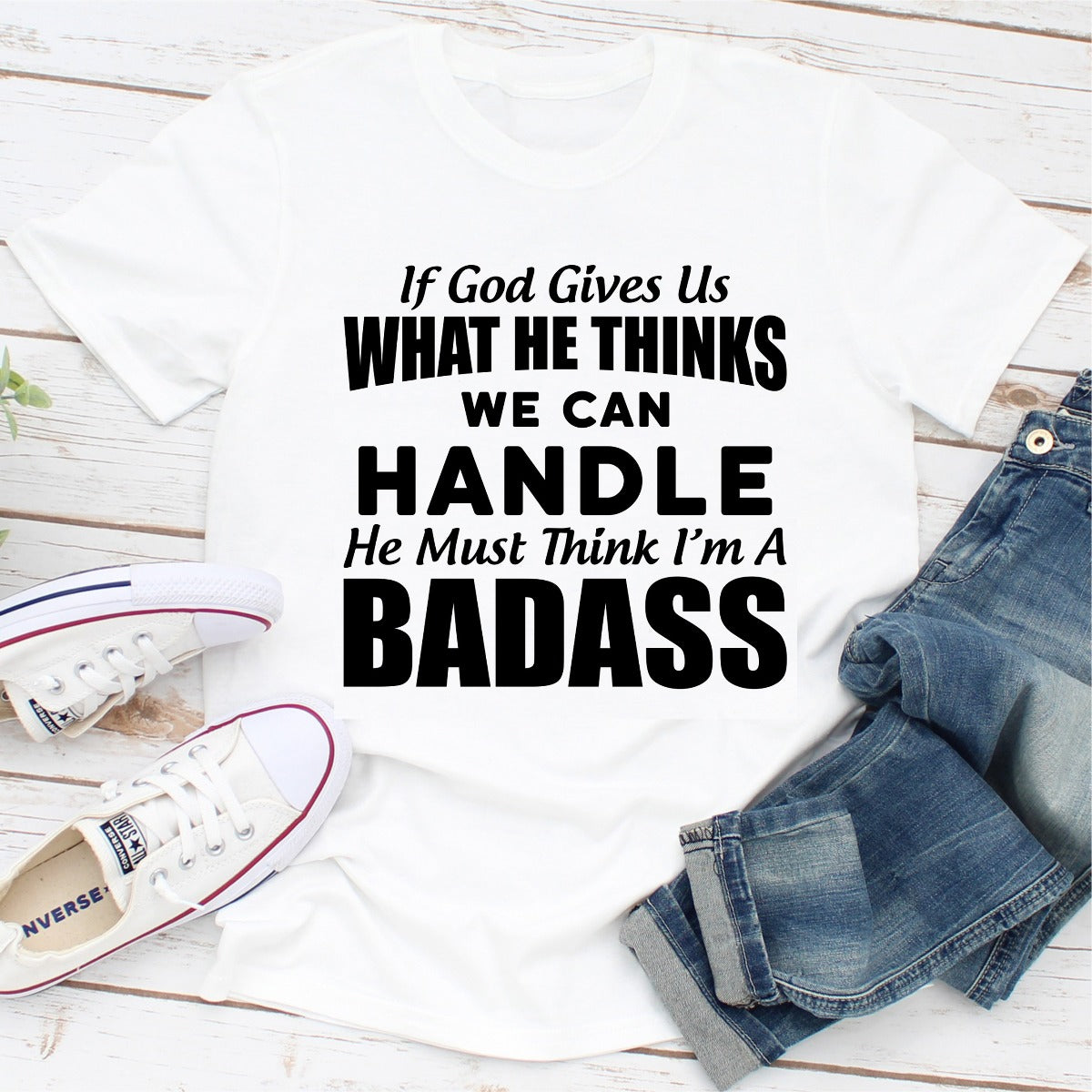 A stylish black t-shirt featuring the phrase 'If God Give Us What He Think We Can Handle He Must Think I'm A Badass' in bold lettering.