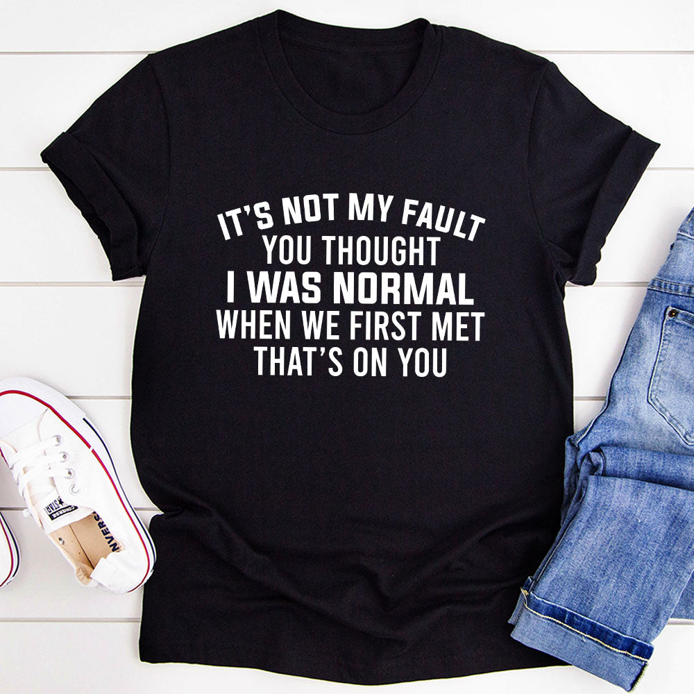 A stylish black t-shirt featuring the phrase 'It’s Not My Fault You Thought I Was Normal' printed in bold letters, showcasing its soft fabric and durable stitching.