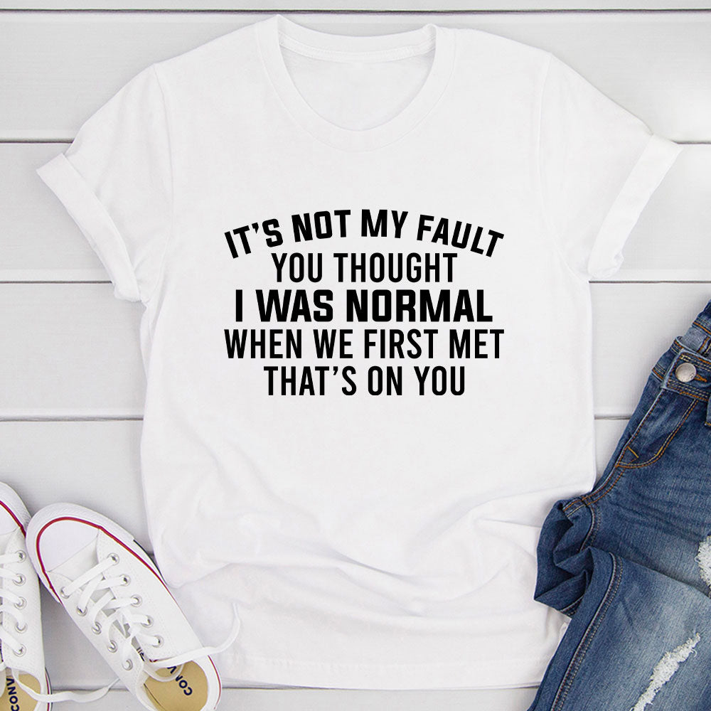 A stylish black t-shirt featuring the phrase 'It’s Not My Fault You Thought I Was Normal' printed in bold letters, showcasing its soft fabric and durable stitching.