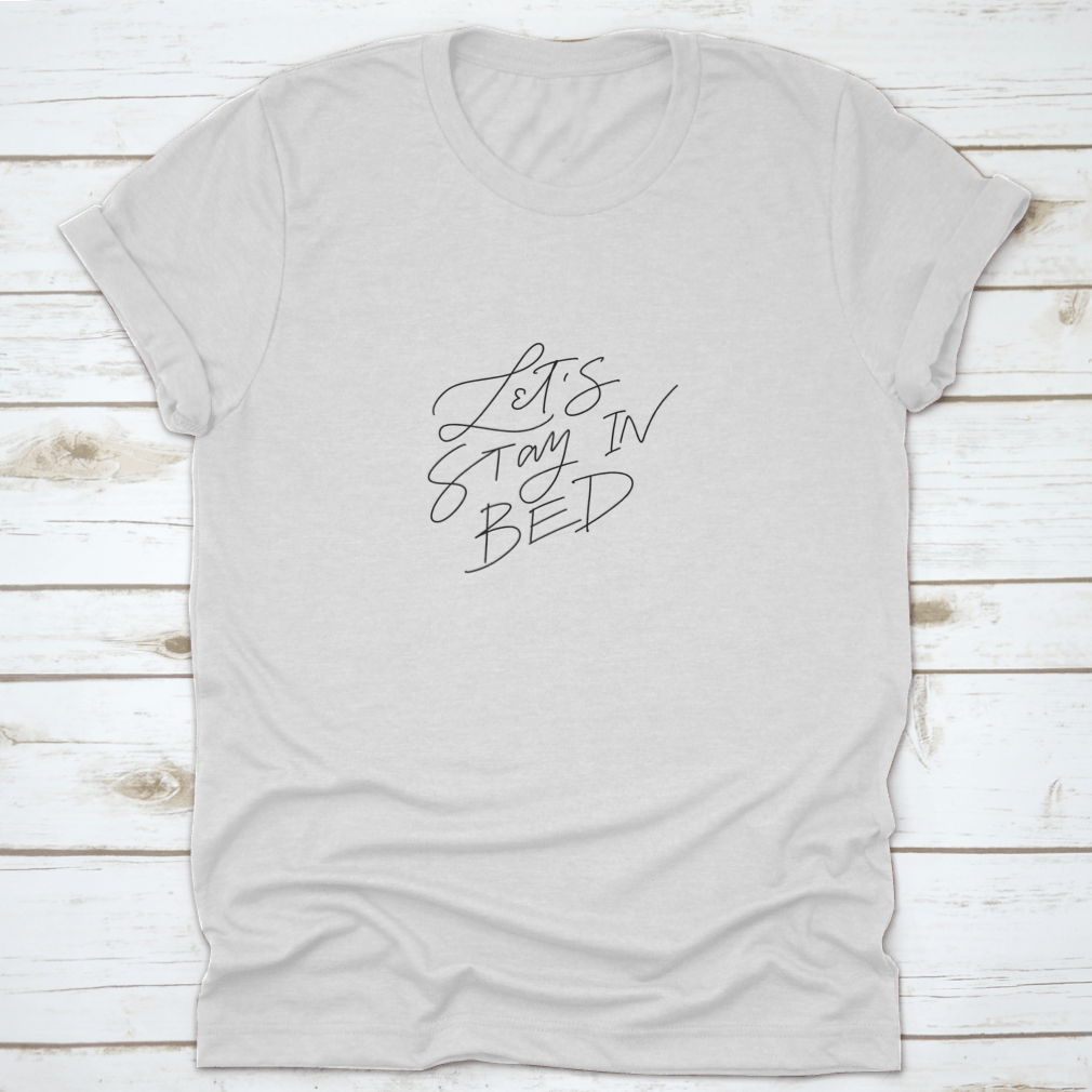 A cozy shirt featuring 'Let's Stay In Bed' vector hand lettering typography, made from 100% cotton for ultimate comfort.