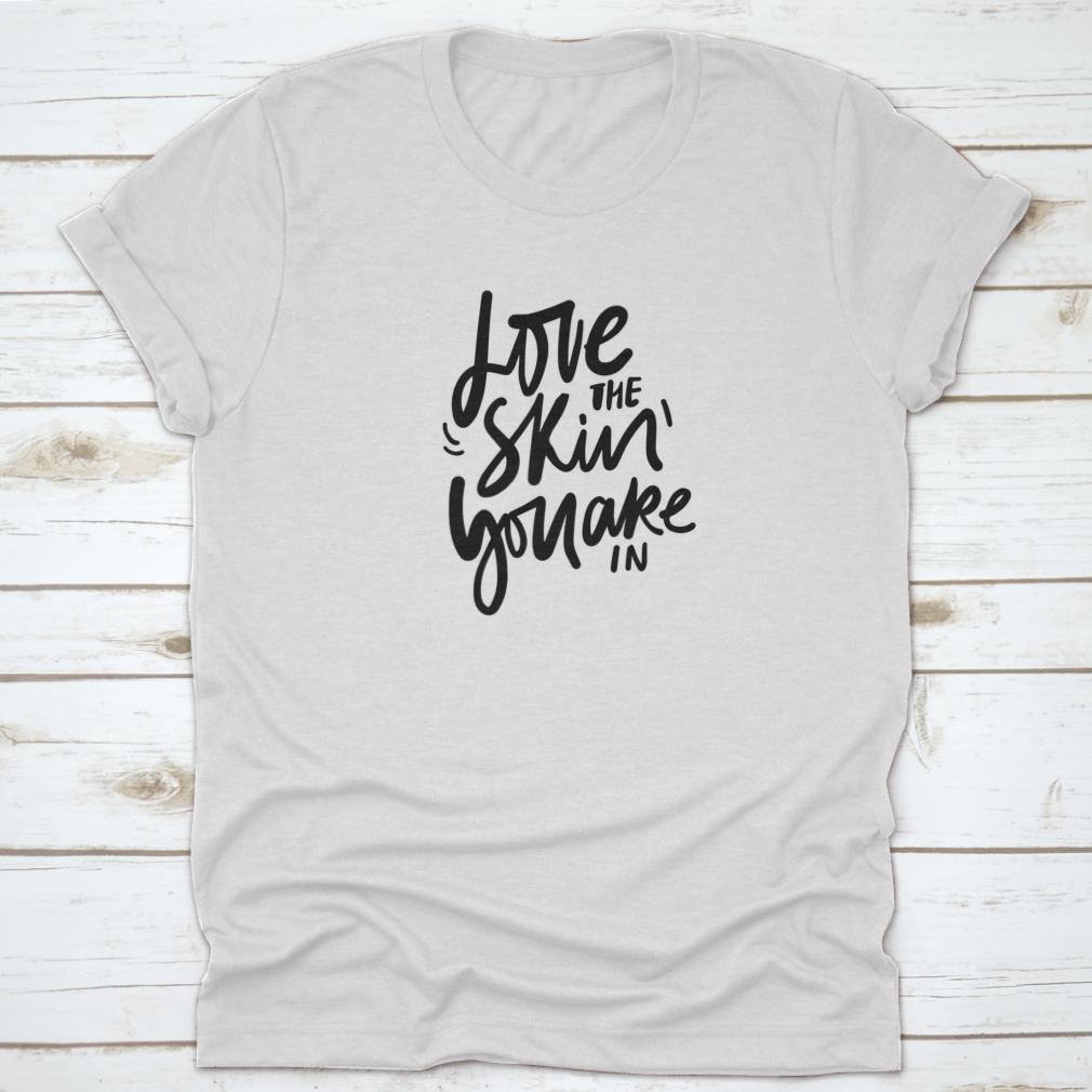 A stylish calligraphic shirt design featuring the quote 'Love Your Skin You Are In', made from soft cotton fabric.