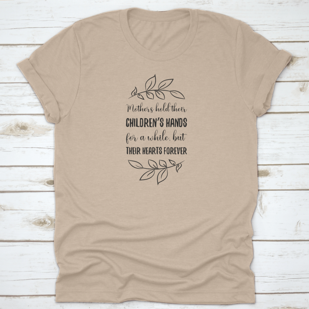 A soft cotton t-shirt featuring the phrase 'Mothers Hold Their Children’s Hands For A While, But Their Hearts', showcasing a classic fit and durable design.