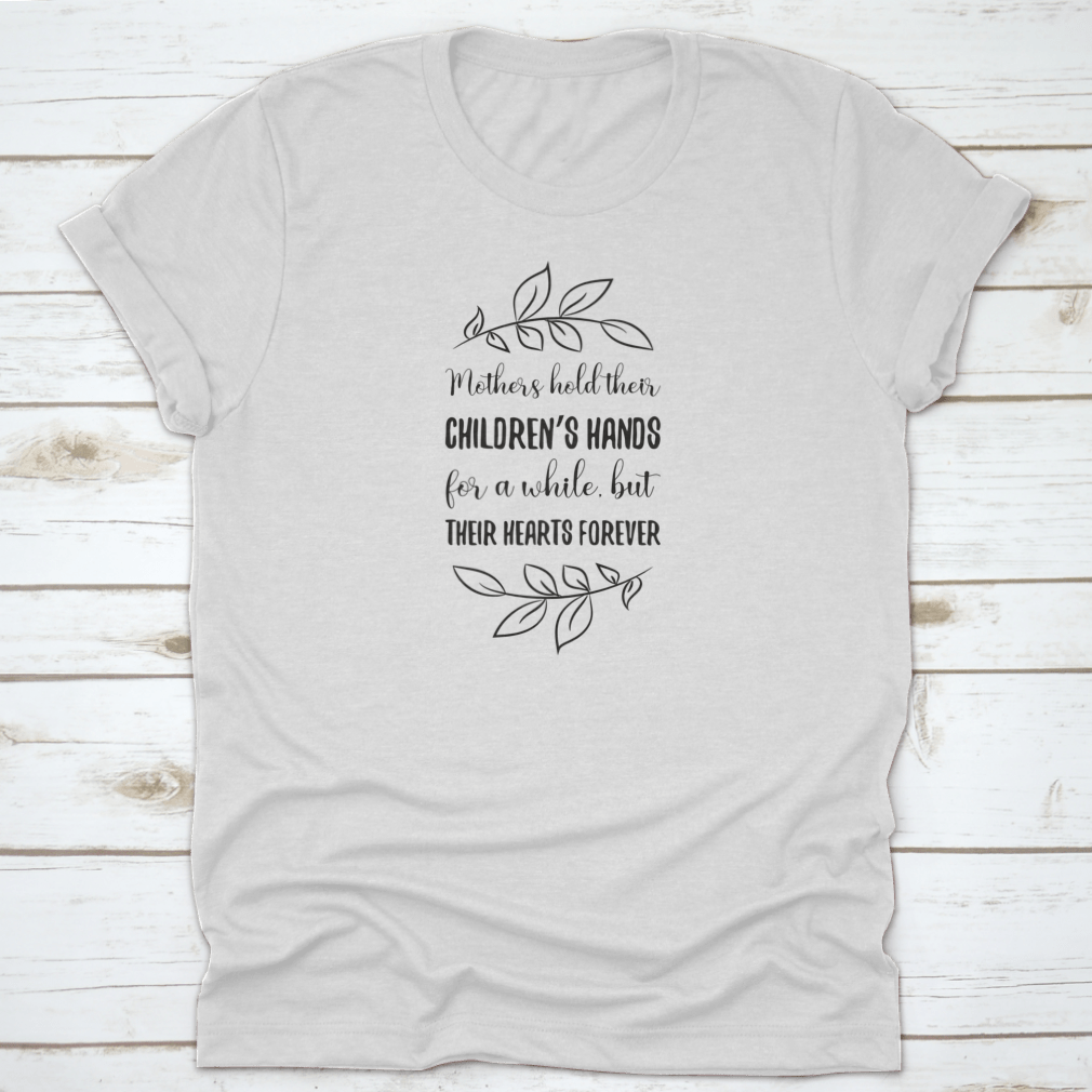 A soft cotton t-shirt featuring the phrase 'Mothers Hold Their Children’s Hands For A While, But Their Hearts', showcasing a classic fit and durable design.