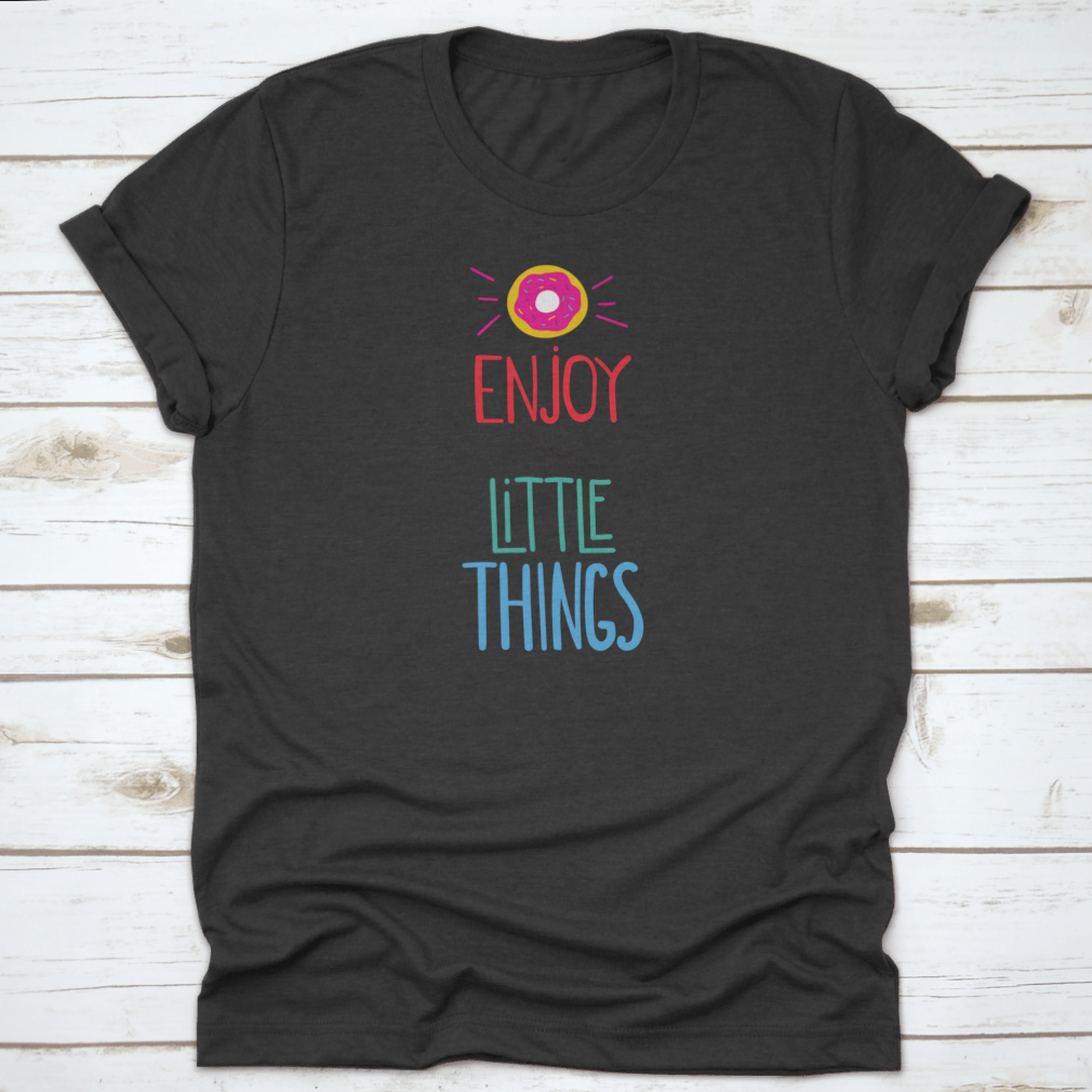 Motivational quote shirt featuring 'Enjoy The Little Things' in a stylish font, displayed with a donut for a fun touch.