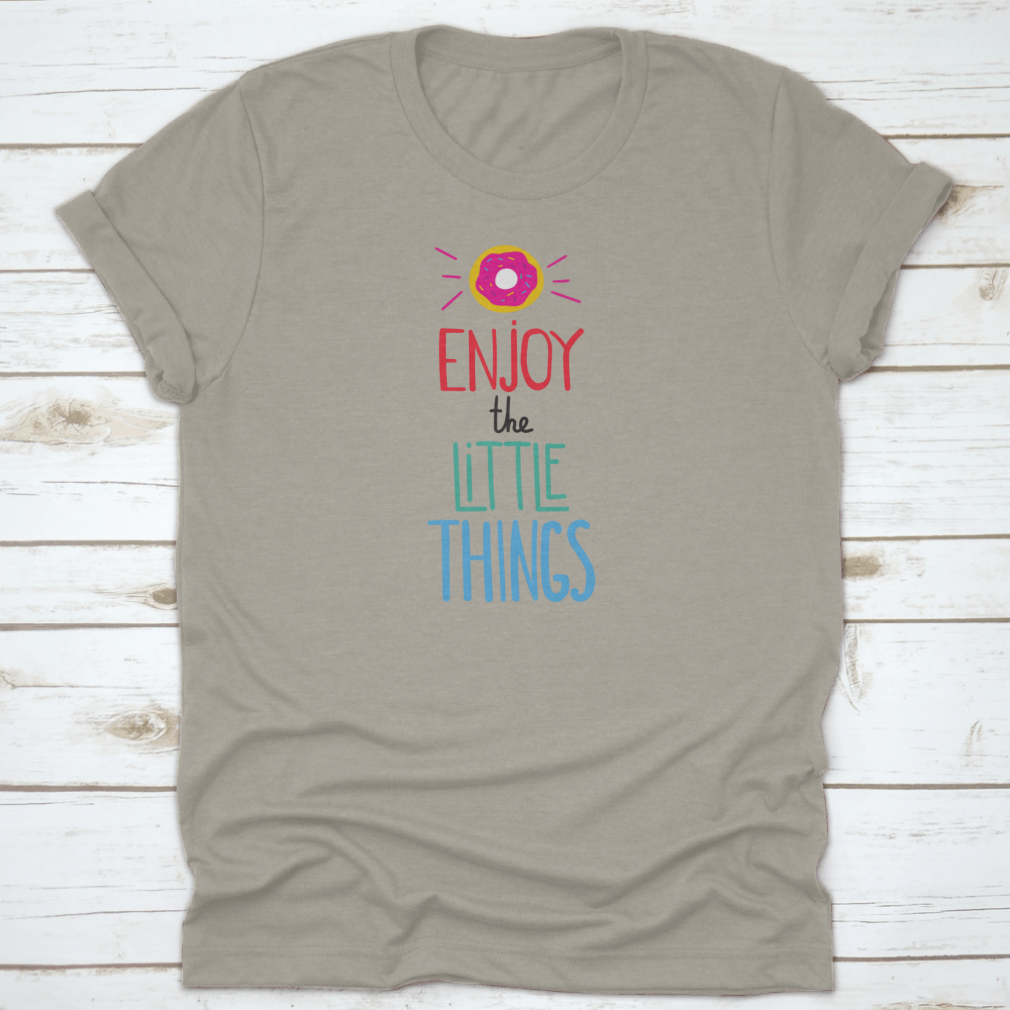 Motivational quote shirt featuring 'Enjoy The Little Things' in a stylish font, displayed with a donut for a fun touch.