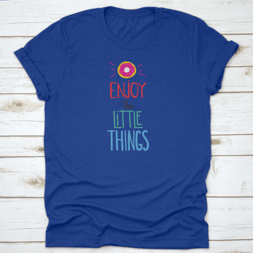 Motivational quote shirt featuring 'Enjoy The Little Things' in a stylish font, displayed with a donut for a fun touch.