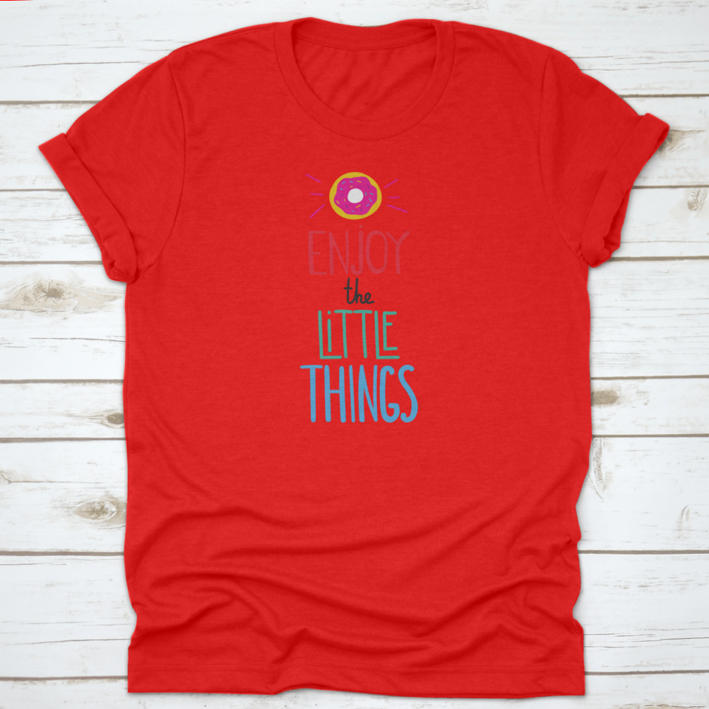 Motivational quote shirt featuring 'Enjoy The Little Things' in a stylish font, displayed with a donut for a fun touch.