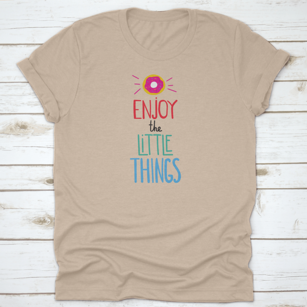 Motivational quote shirt featuring 'Enjoy The Little Things' in a stylish font, displayed with a donut for a fun touch.