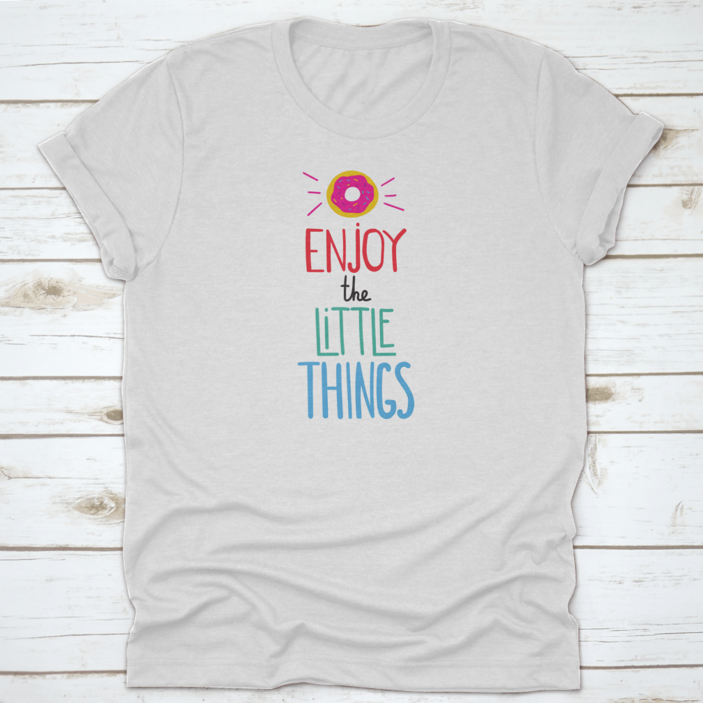 Motivational quote shirt featuring 'Enjoy The Little Things' in a stylish font, displayed with a donut for a fun touch.