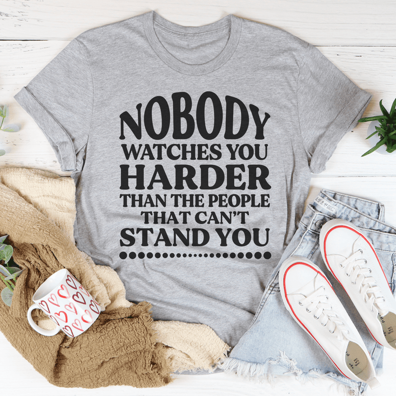 A stylish black t-shirt featuring the phrase 'Nobody Watches You Harder Than The People That Can't Stand You' in bold white lettering.