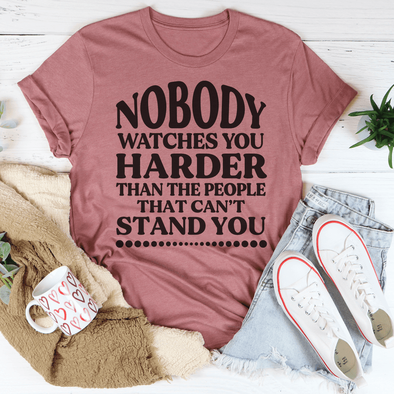 A stylish black t-shirt featuring the phrase 'Nobody Watches You Harder Than The People That Can't Stand You' in bold white lettering.