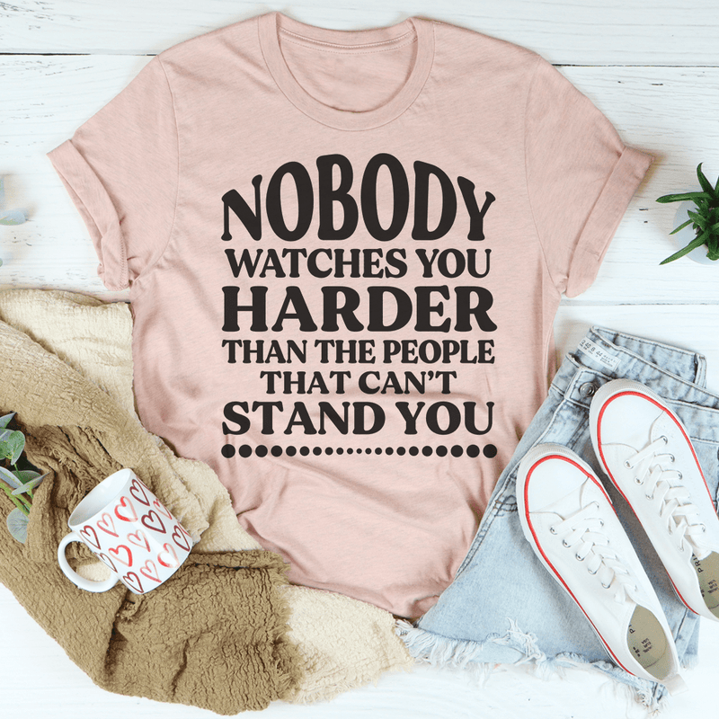 A stylish black t-shirt featuring the phrase 'Nobody Watches You Harder Than The People That Can't Stand You' in bold white lettering.