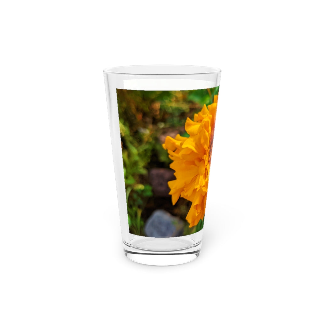 A clear 16oz pint glass featuring an elegant orange flower design, perfect for beverages.