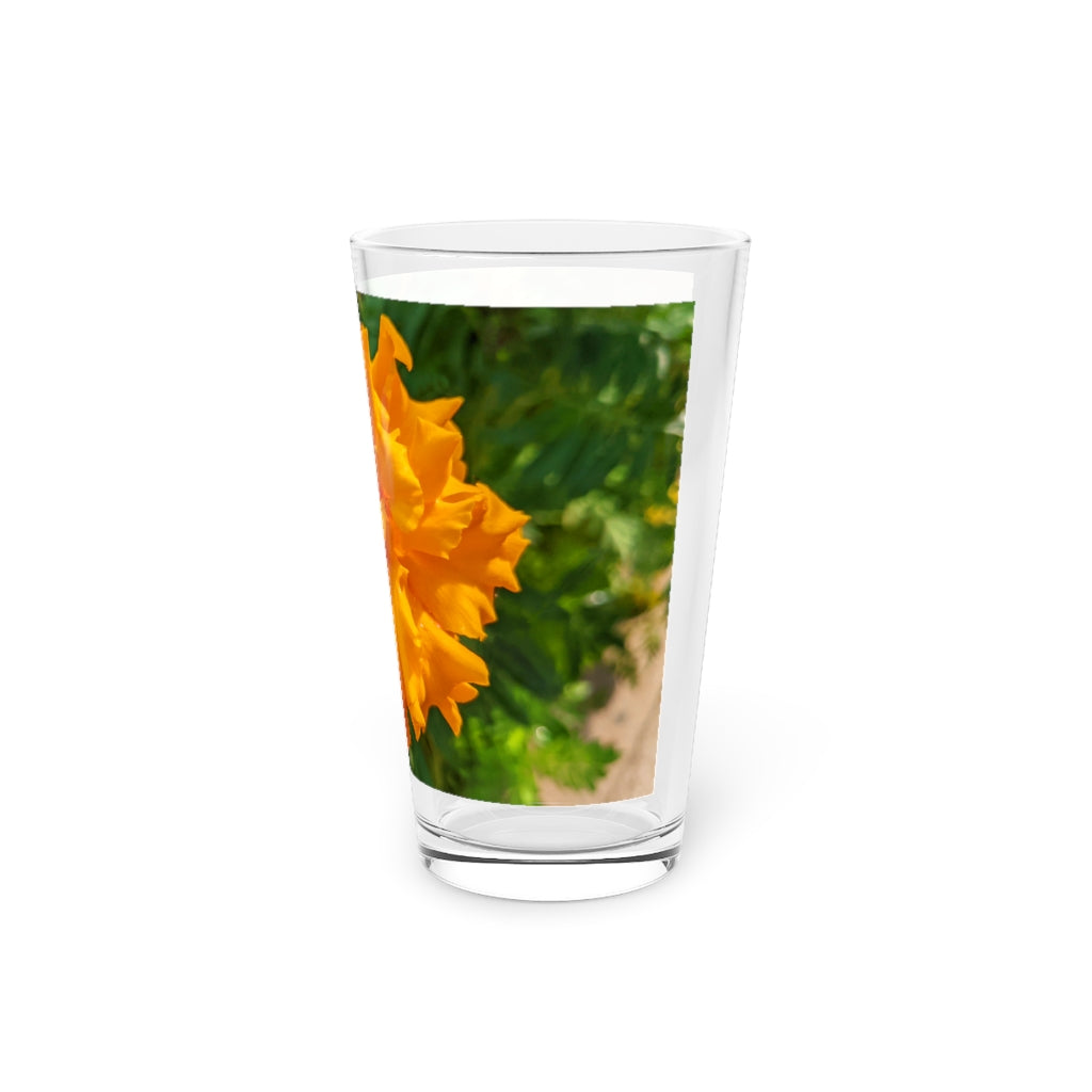 A clear 16oz pint glass featuring an elegant orange flower design, perfect for beverages.