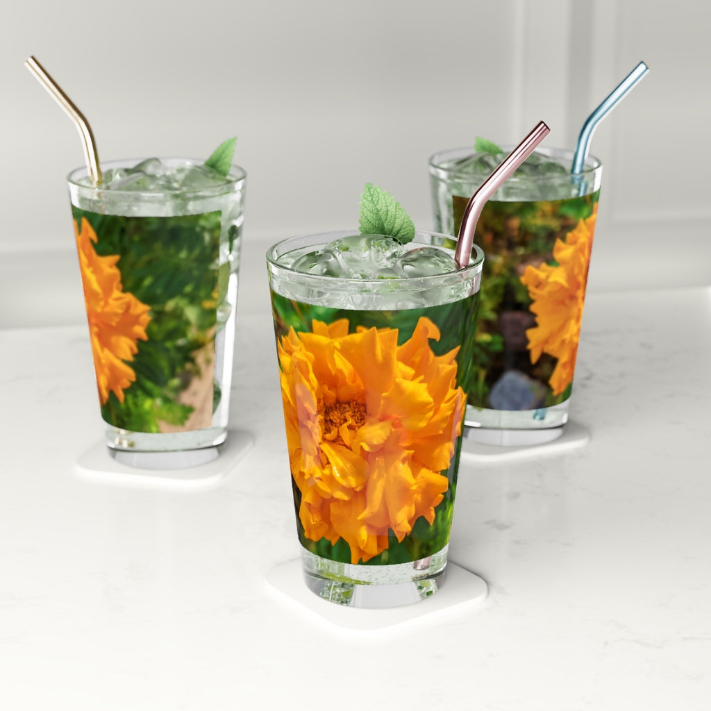 A clear 16oz pint glass featuring an elegant orange flower design, perfect for beverages.