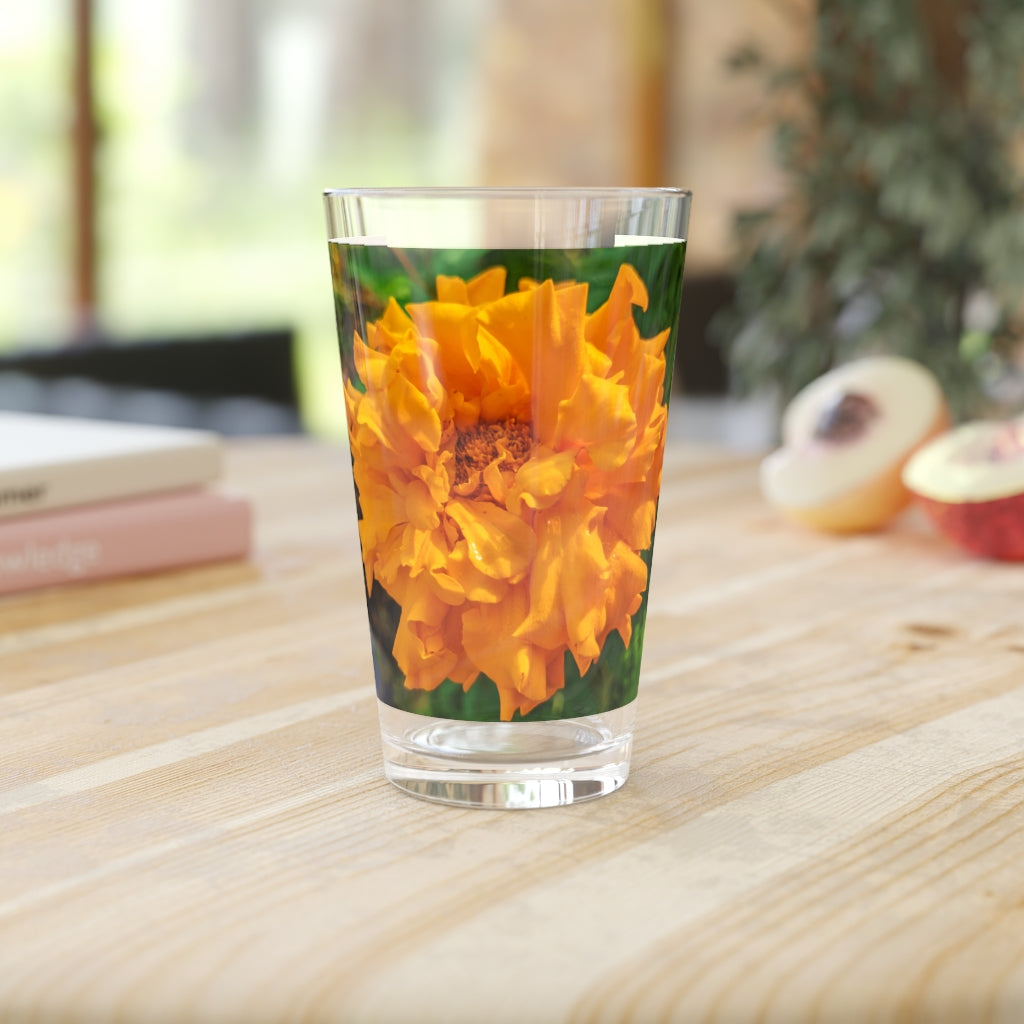 A clear 16oz pint glass featuring an elegant orange flower design, perfect for beverages.