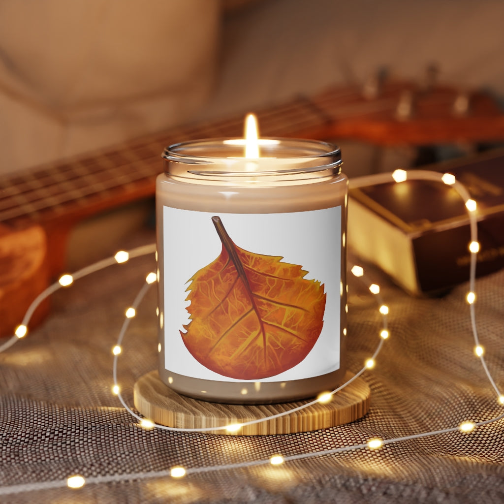 A hand-poured Orange Leaf Scented Candle in a glass container, showcasing its vibrant color and elegant design.