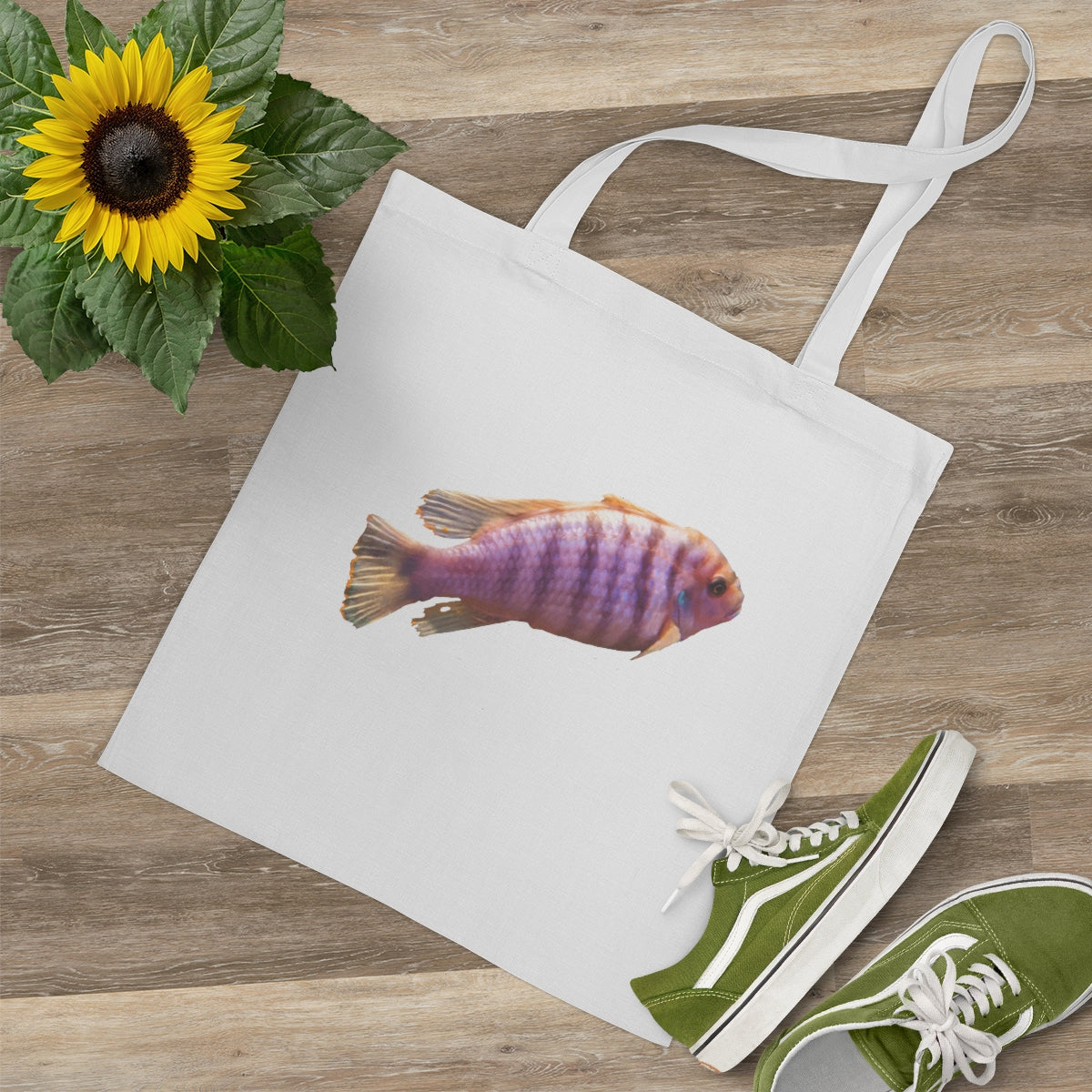 A vibrant purple tote bag featuring a colorful fish design, made from 100% cotton with long cross-stitched handles for durability.