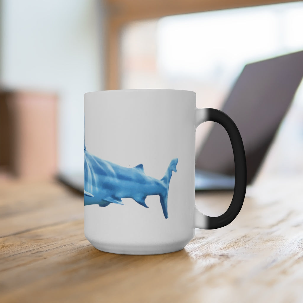 A white ceramic mug featuring a shark design that changes color when filled with hot liquid, showcasing its playful and magical feature.