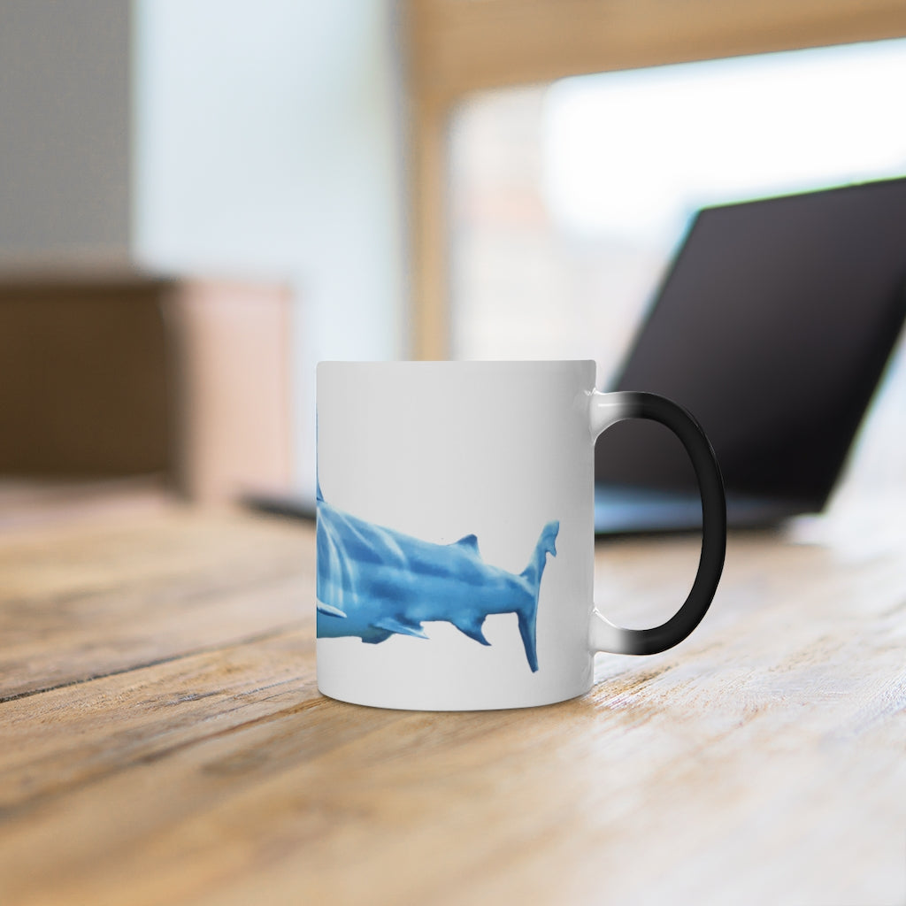 A white ceramic mug featuring a shark design that changes color when filled with hot liquid, showcasing its playful and magical feature.