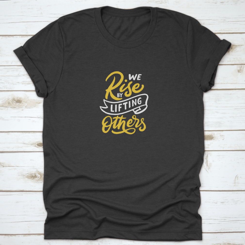 A motivational T-shirt featuring the quote 'We Rise By Lifting Others', made from soft cotton fabric, displayed on a neutral background.