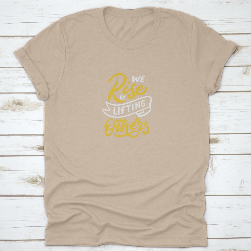 A motivational T-shirt featuring the quote 'We Rise By Lifting Others', made from soft cotton fabric, displayed on a neutral background.