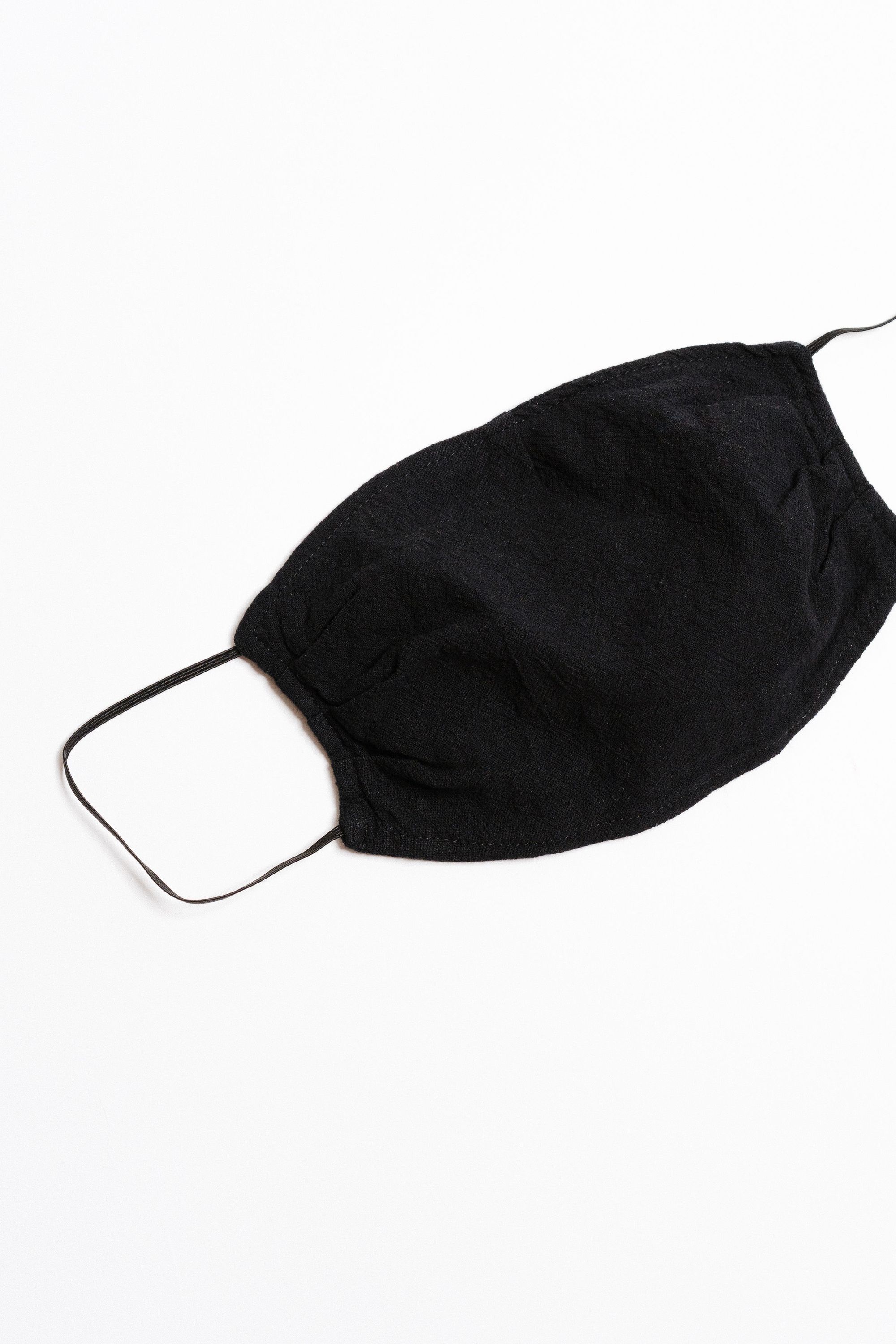 Black textured face mask with black elastic ear straps, designed for comfort and safety, featuring a pocket for filter insertion.