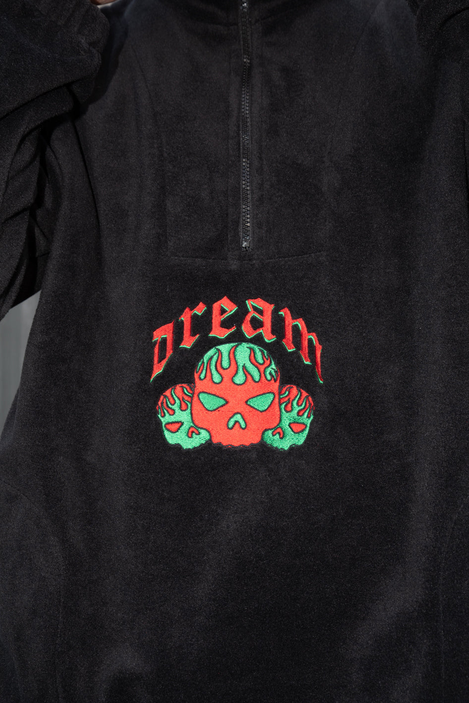 Black fleece jacket with flaming skull embroidery, featuring a 1/4 zip and two front pockets.