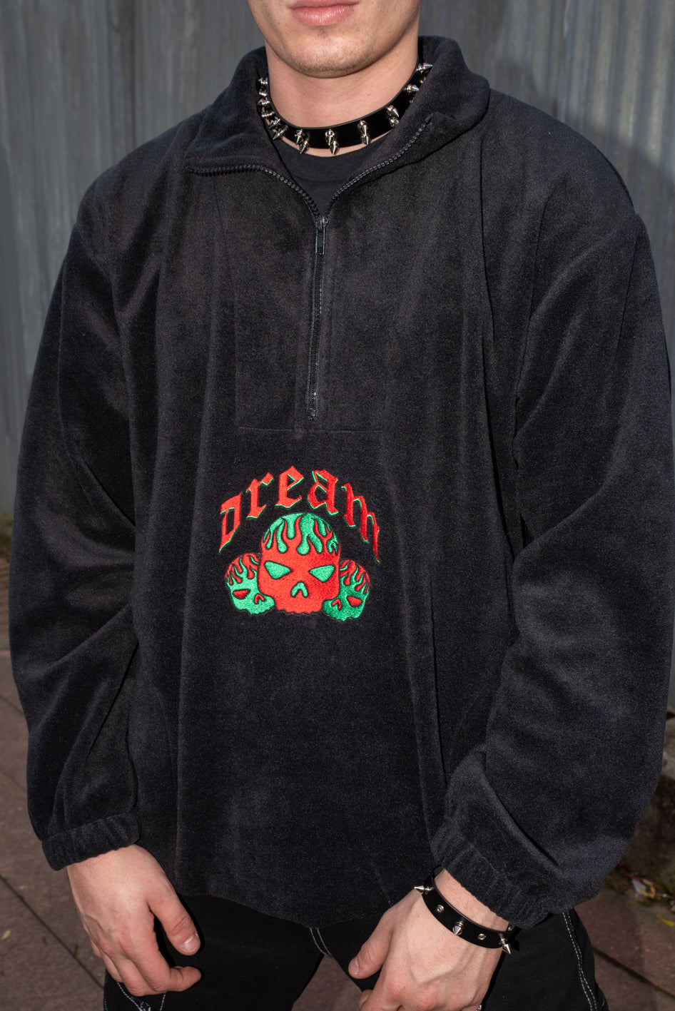 Black fleece jacket with flaming skull embroidery, featuring a 1/4 zip and two front pockets.