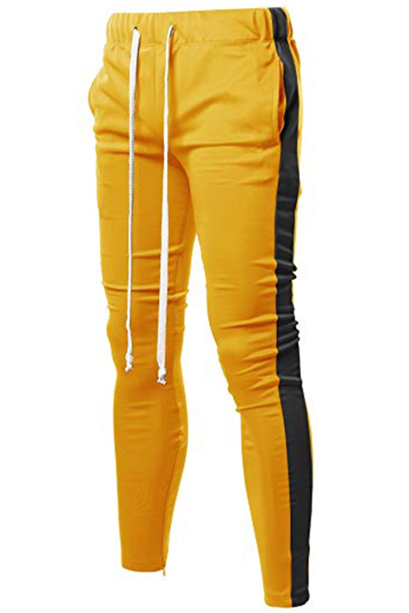 A pair of yellow and black Holiday track pants featuring a bold side stripe, adjustable elastic waistband, and sewn-in ankle zippers.