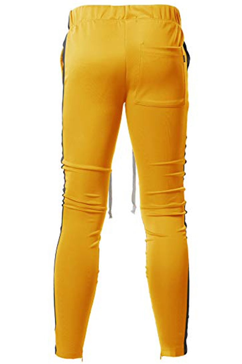 A pair of yellow and black Holiday track pants featuring a bold side stripe, adjustable elastic waistband, and sewn-in ankle zippers.