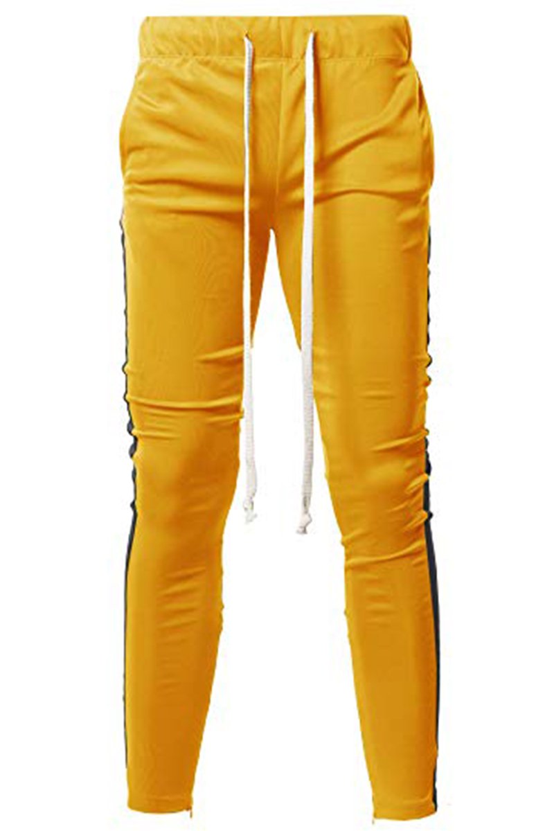 A pair of yellow and black Holiday track pants featuring a bold side stripe, adjustable elastic waistband, and sewn-in ankle zippers.