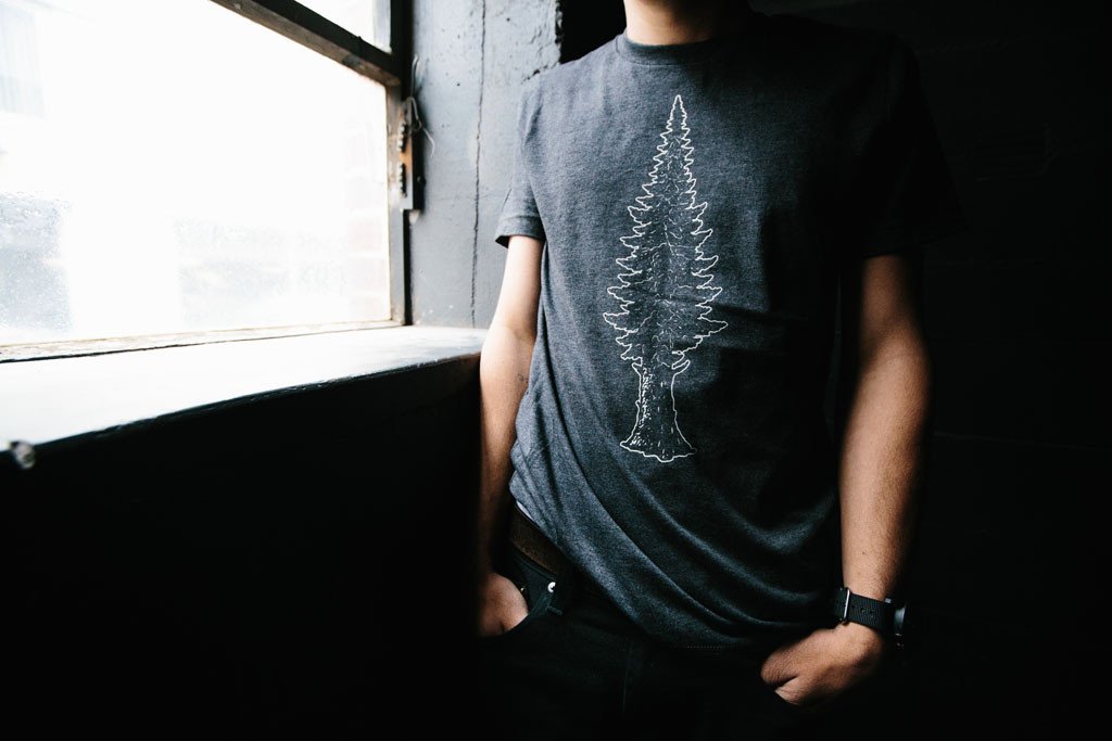 Mighty Pine Tee in dark gray featuring a white screen printed design of a pine tree, made from soft cotton and polyester blend.