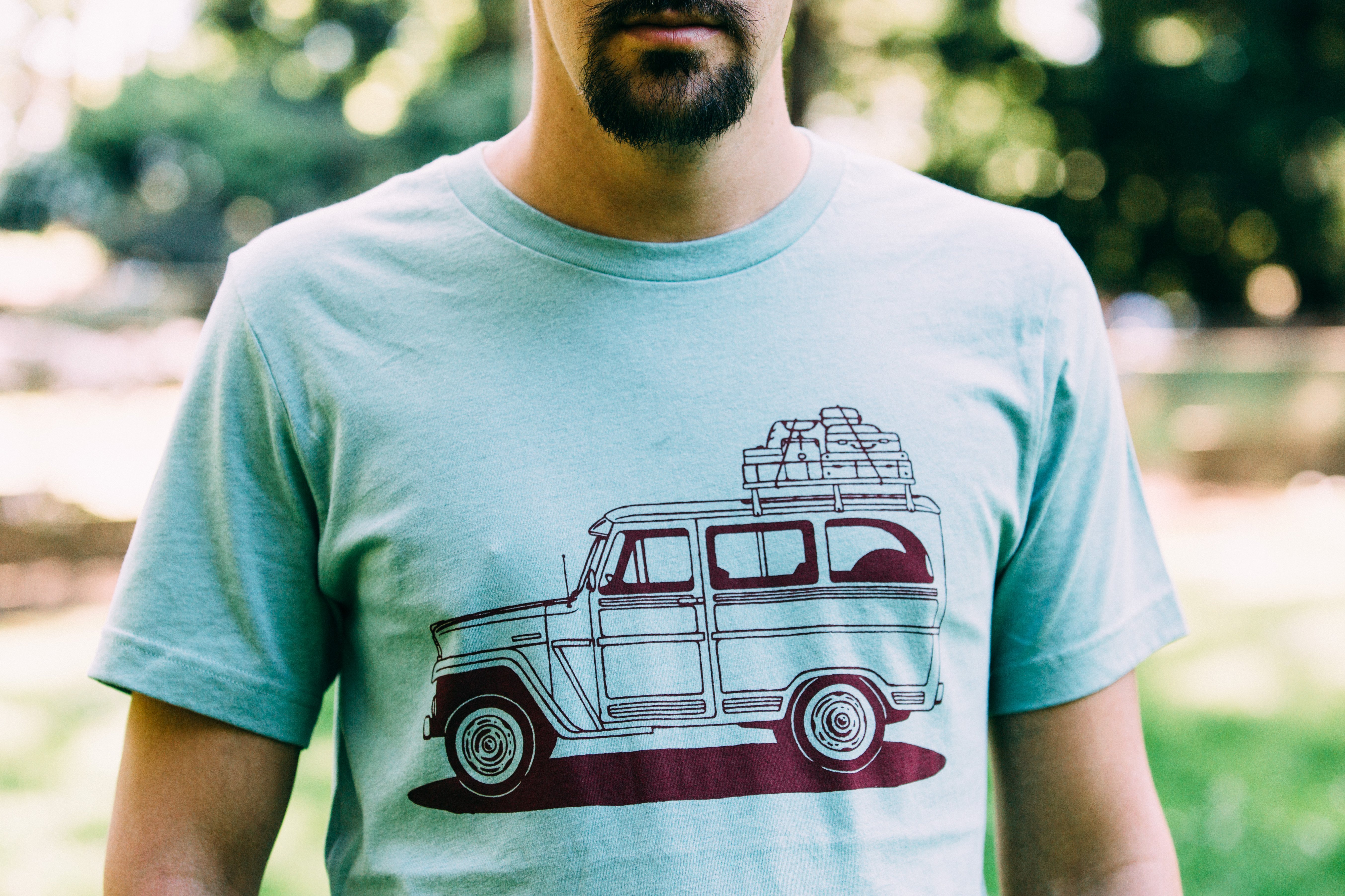 Willy Wagon Tee in dusty blue featuring a classic Jeep design printed in red water-based ink, made from a soft tri-blend fabric.