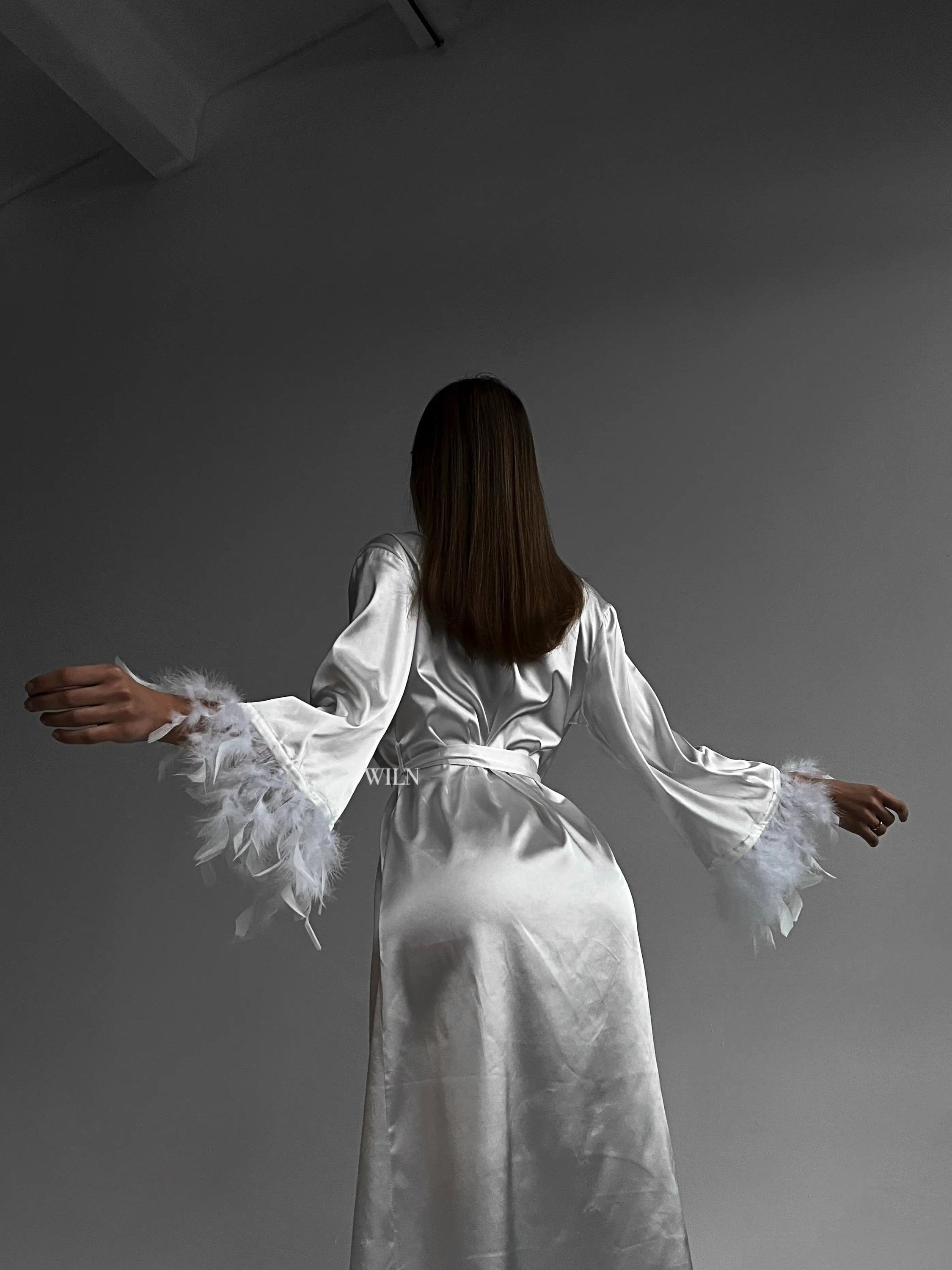 A luxurious white satin robe with flowy long sleeves and feather trim, perfect for bridal occasions.