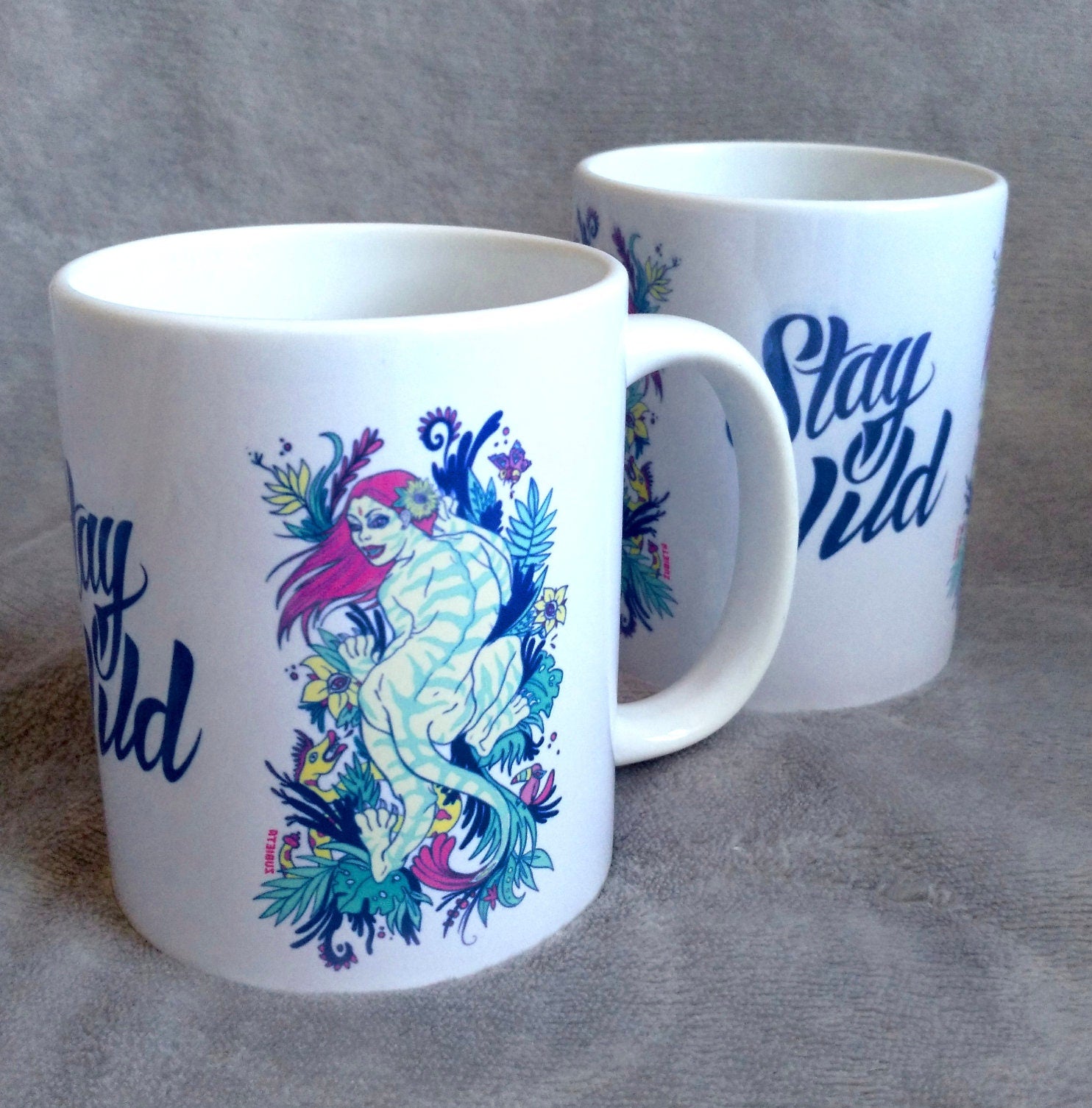 Ceramic mug featuring a vibrant tiger woman design with 'Stay Wild' lettering in the center, showcasing artistic flair.