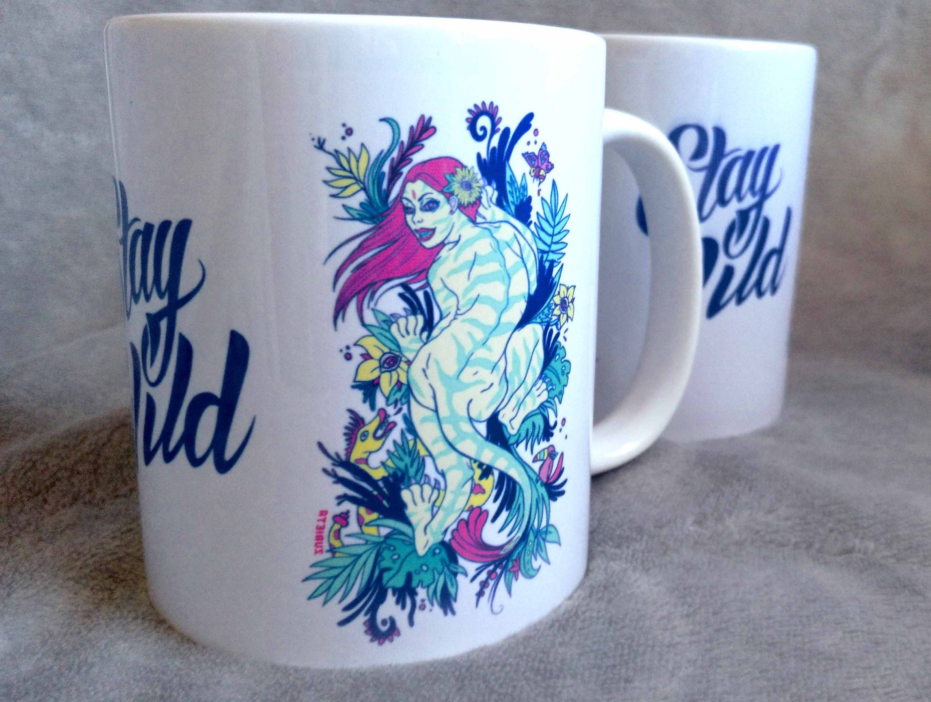 Ceramic mug featuring a vibrant tiger woman design with 'Stay Wild' lettering in the center, showcasing artistic flair.