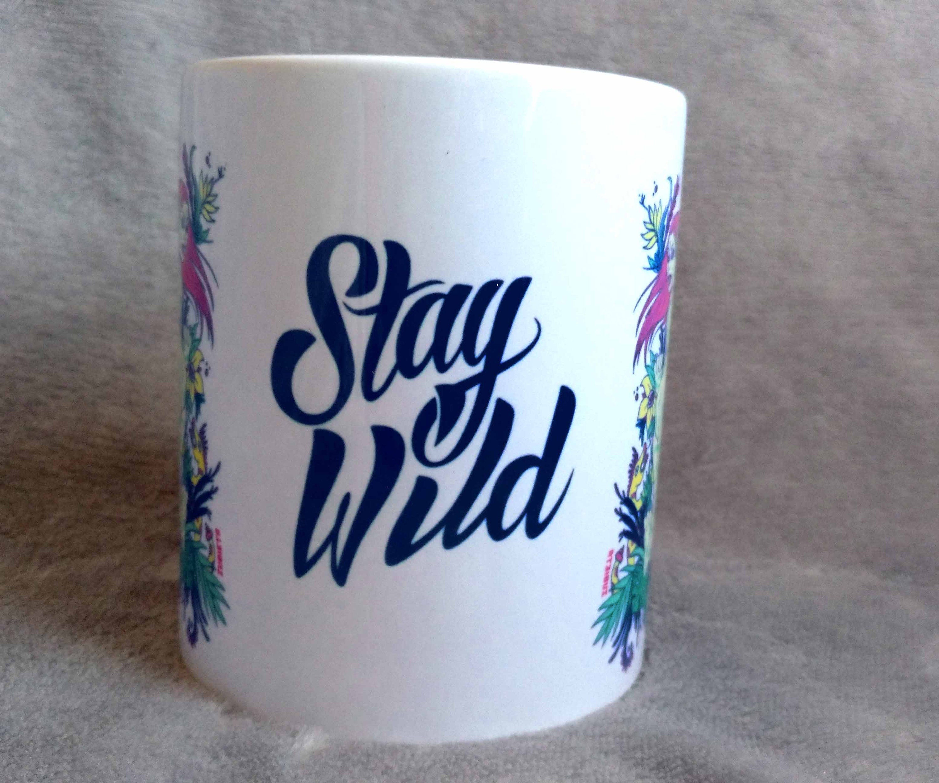 Ceramic mug featuring a vibrant tiger woman design with 'Stay Wild' lettering in the center, showcasing artistic flair.