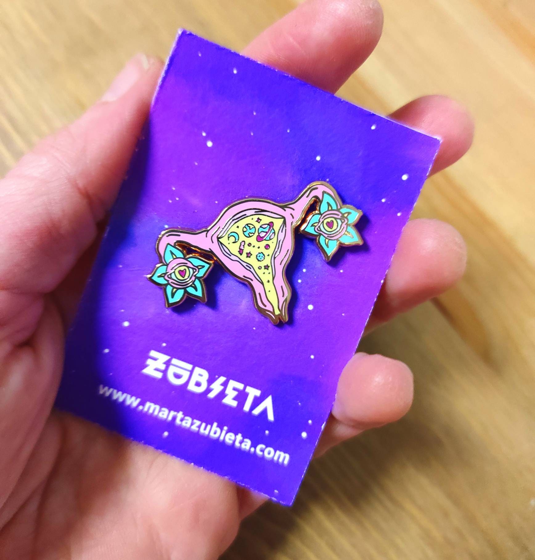 Cosmic uterus enamel pin with rose gold finish, featuring a psychedelic design that celebrates femininity and body positivity.