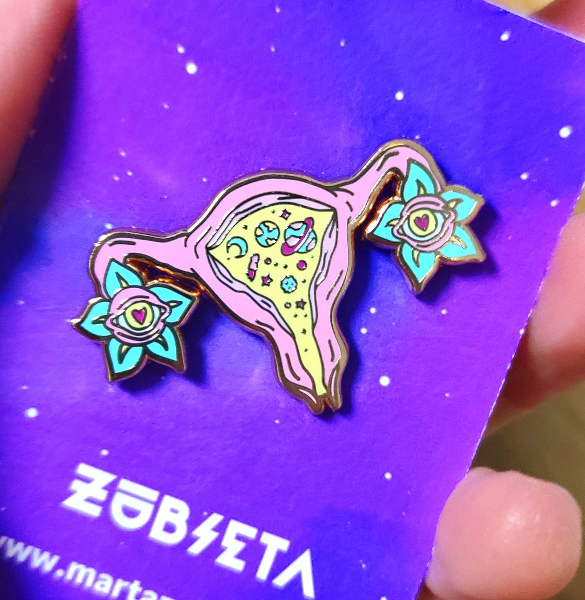 Cosmic uterus enamel pin with rose gold finish, featuring a psychedelic design that celebrates femininity and body positivity.