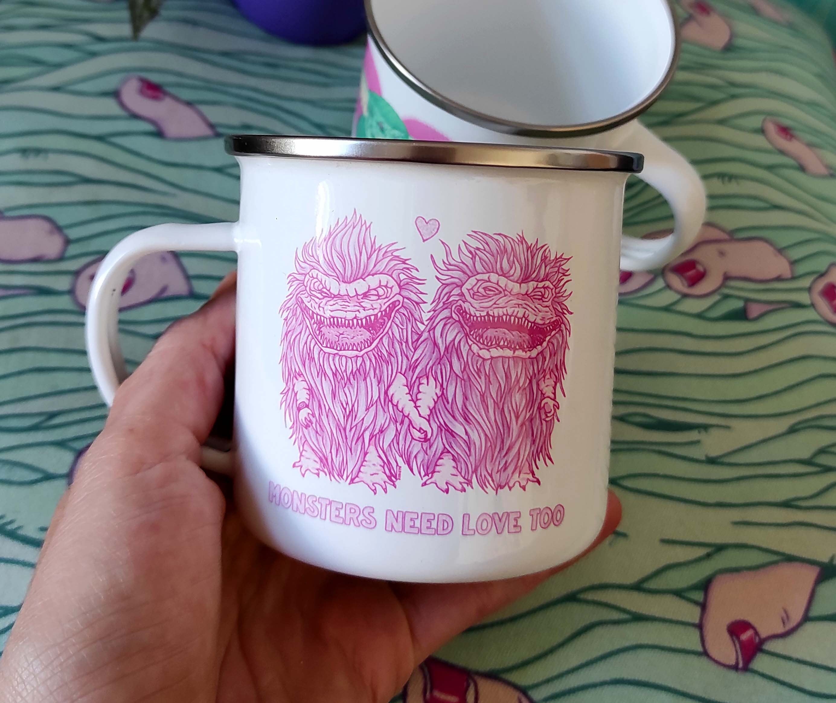 Enamel mug featuring 'Monsters Need Love Too' design inspired by The Critters, made of stainless steel, 10oz capacity.