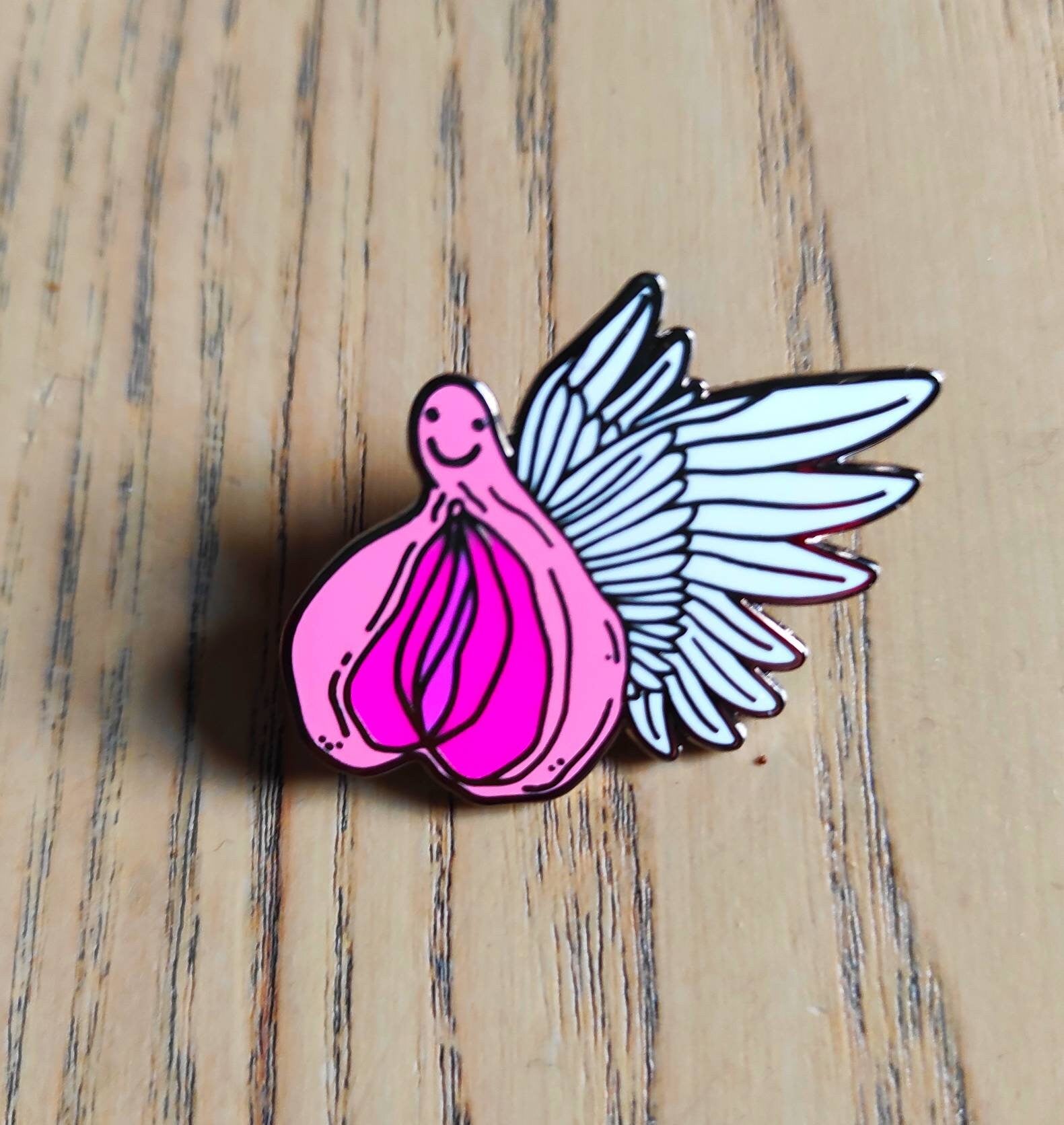 A colorful enamel pin featuring a whimsical design of flying vaginas in space, symbolizing body positivity and empowerment.