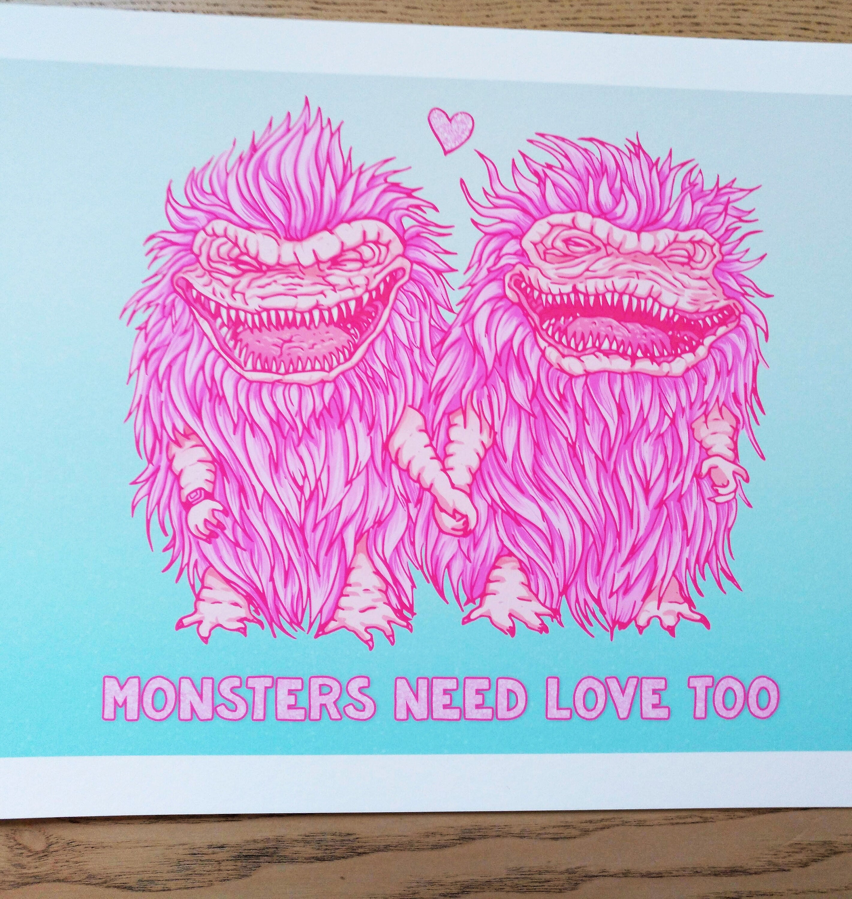 A vibrant gicleé print titled 'Monsters Need Love Too', featuring whimsical monsters inspired by The Critters movie, with a handwritten signature.