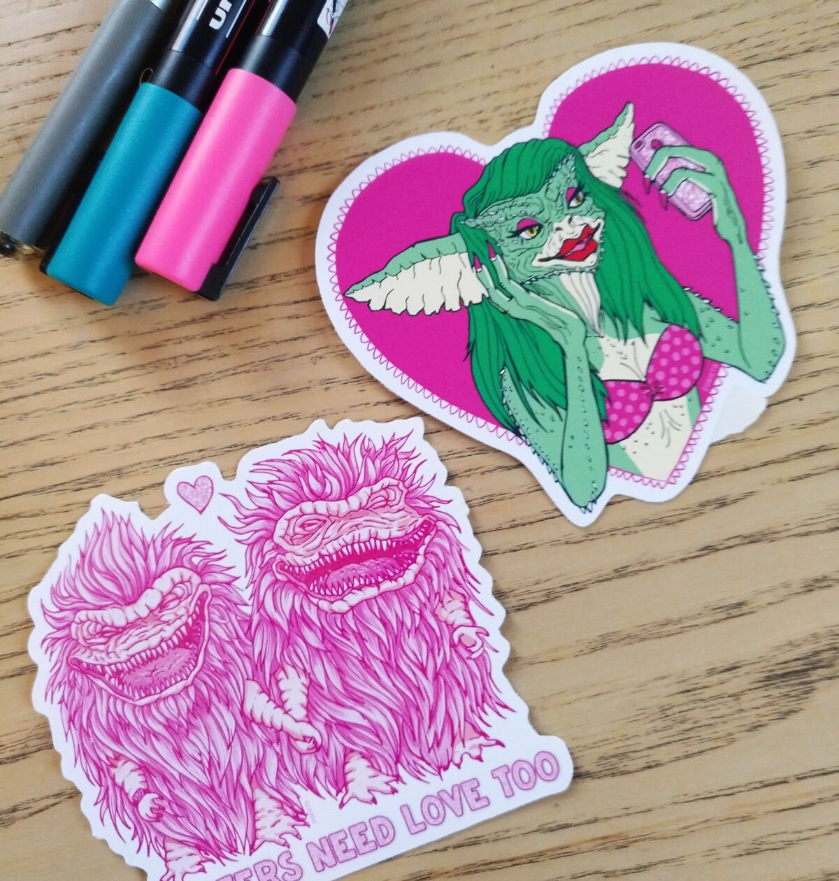 A pack of two colorful vinyl stickers featuring Greta the Gremlin and the phrase Monsters Need Love Too, perfect for 80's horror movie fans.