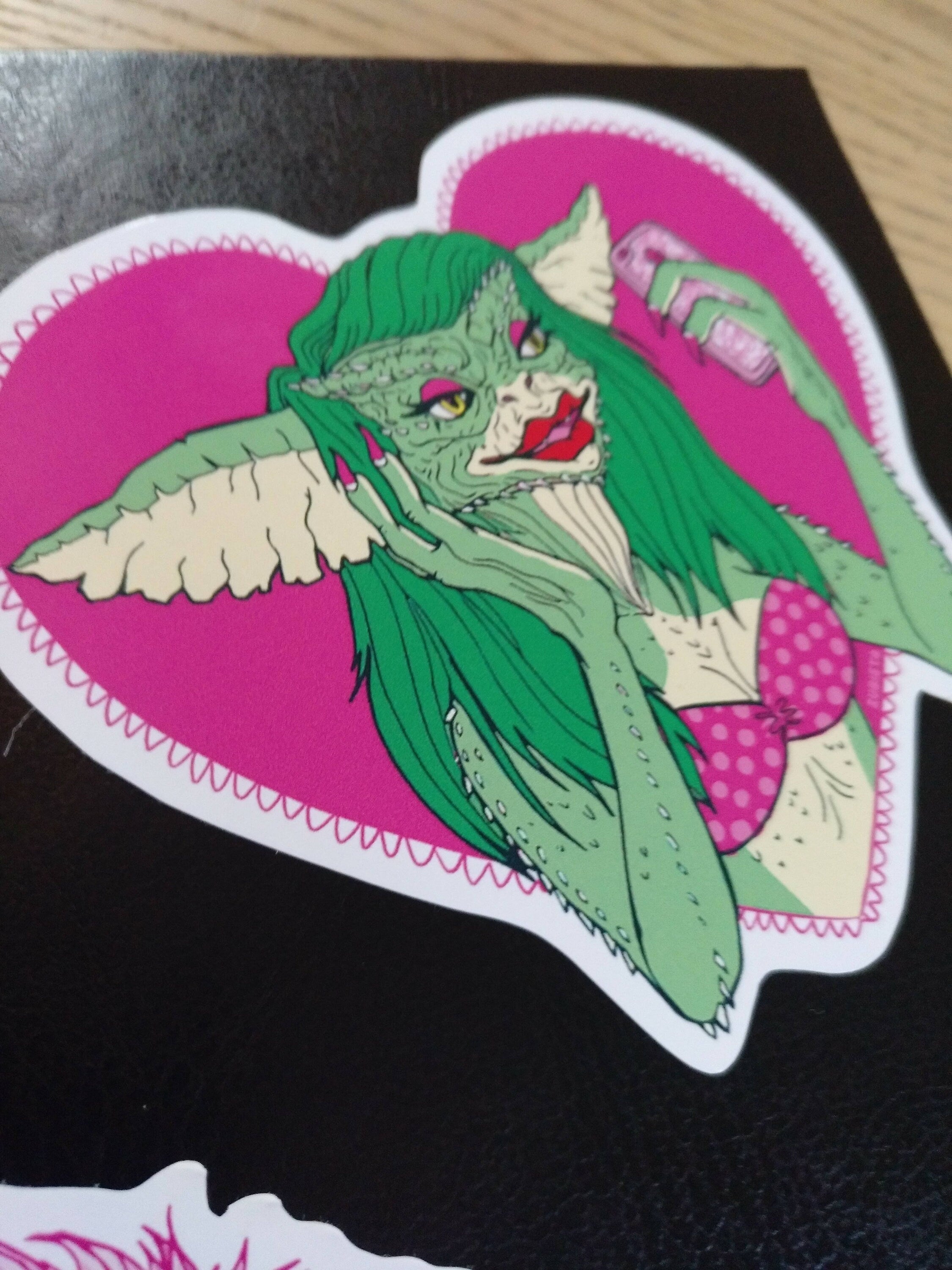 A pack of two colorful vinyl stickers featuring Greta the Gremlin and the phrase Monsters Need Love Too, perfect for 80's horror movie fans.