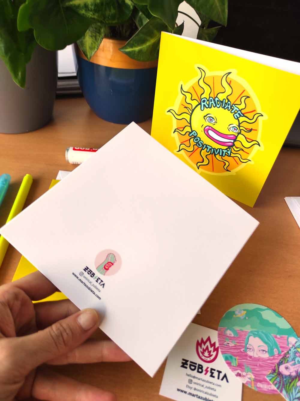 A vibrant psychedelic card titled 'Radiate Positivity', featuring colorful designs symbolizing love and friendship, with a square envelope and sticker.