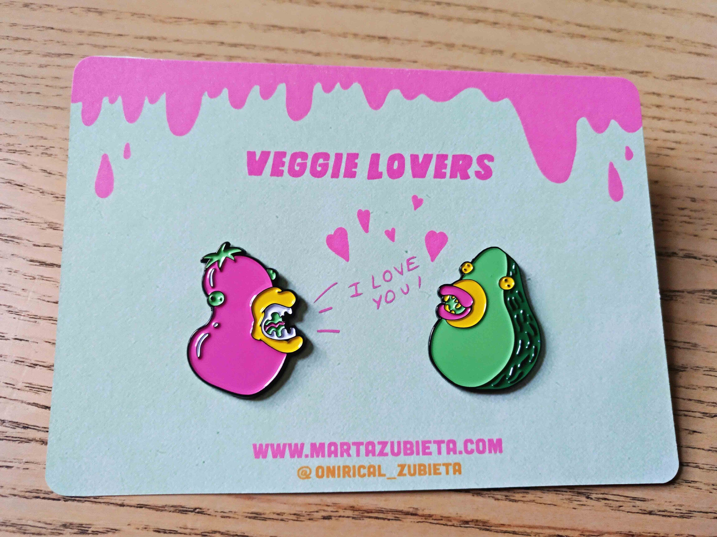 A colorful enamel pin pack featuring avocado and aubergine designs, made from black metal with soft enamel colors.