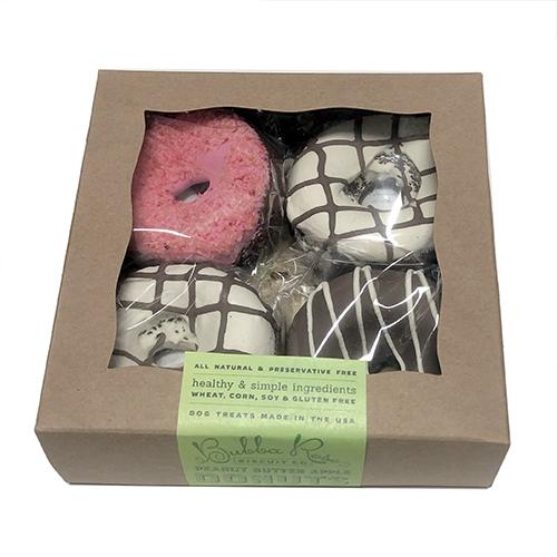 A colorful donut gift box containing four soft peanut butter apple cake donuts for dogs, topped with yogurt coating.