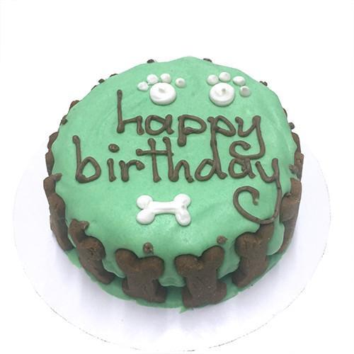 A beautifully decorated Green Dog Cake featuring a soft peanut butter banana base, topped with a hard yogurt coating and colorful vegetable decorations, presented in a windowed cake box.